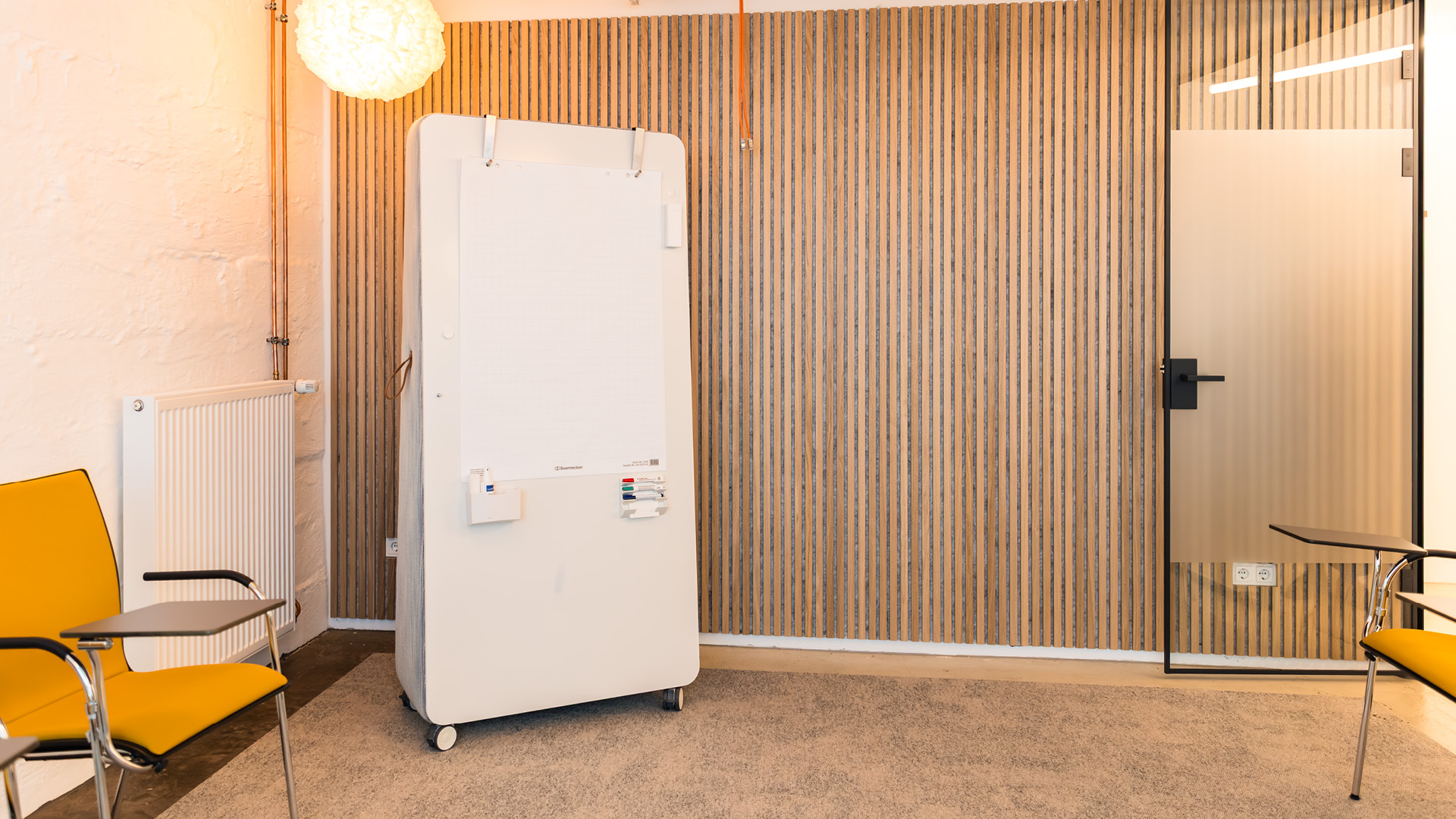 Seminar- und Schulungsraum der APV Münster mit Akustiklamellenwand, flexibler Möblierung und beschreibbarem Whiteboard für Aus- und Weiterbildung.
