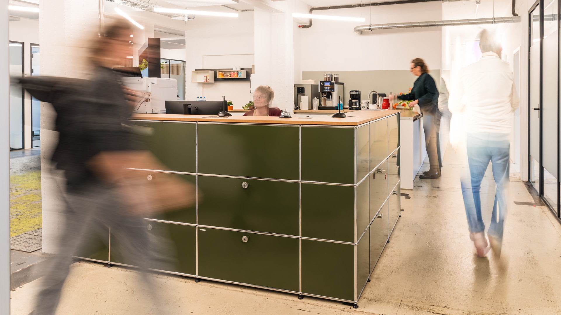 Zentraler Aufenthaltsbereich der APV Münster mit Kaffeebar und USM-Haller-Theke als Treffpunkt für Austausch und informelle Begegnungen.