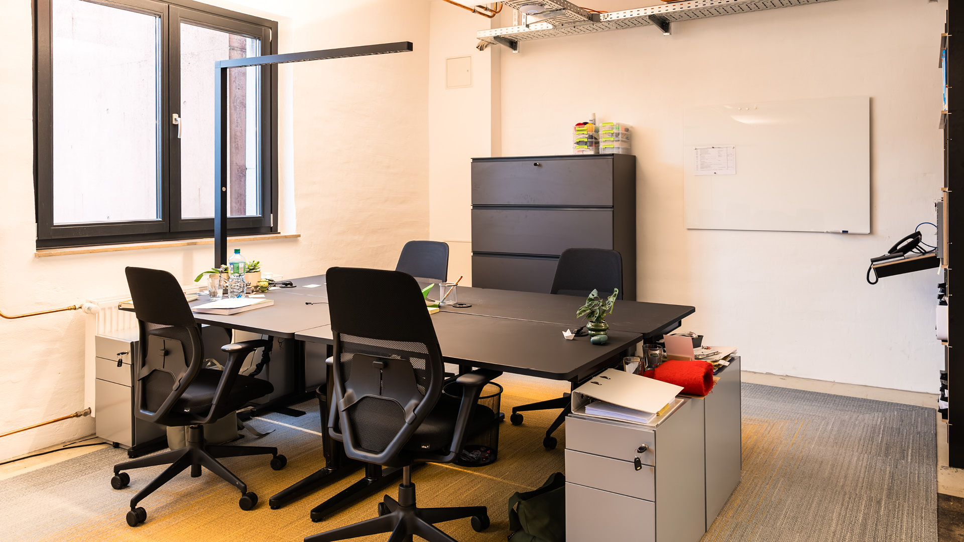 Arbeitsplatz der APV Münster mit höhenverstellbaren Schreibtischen, Whiteboard und sichtbaren Elementen des industriellen Bestands.