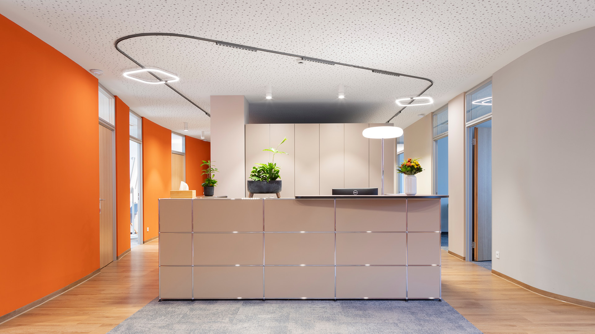 Empfangsbereich mit USM Haller Empfangstheke, orangefarbenen Wänden und geschwungener Lichtführung.