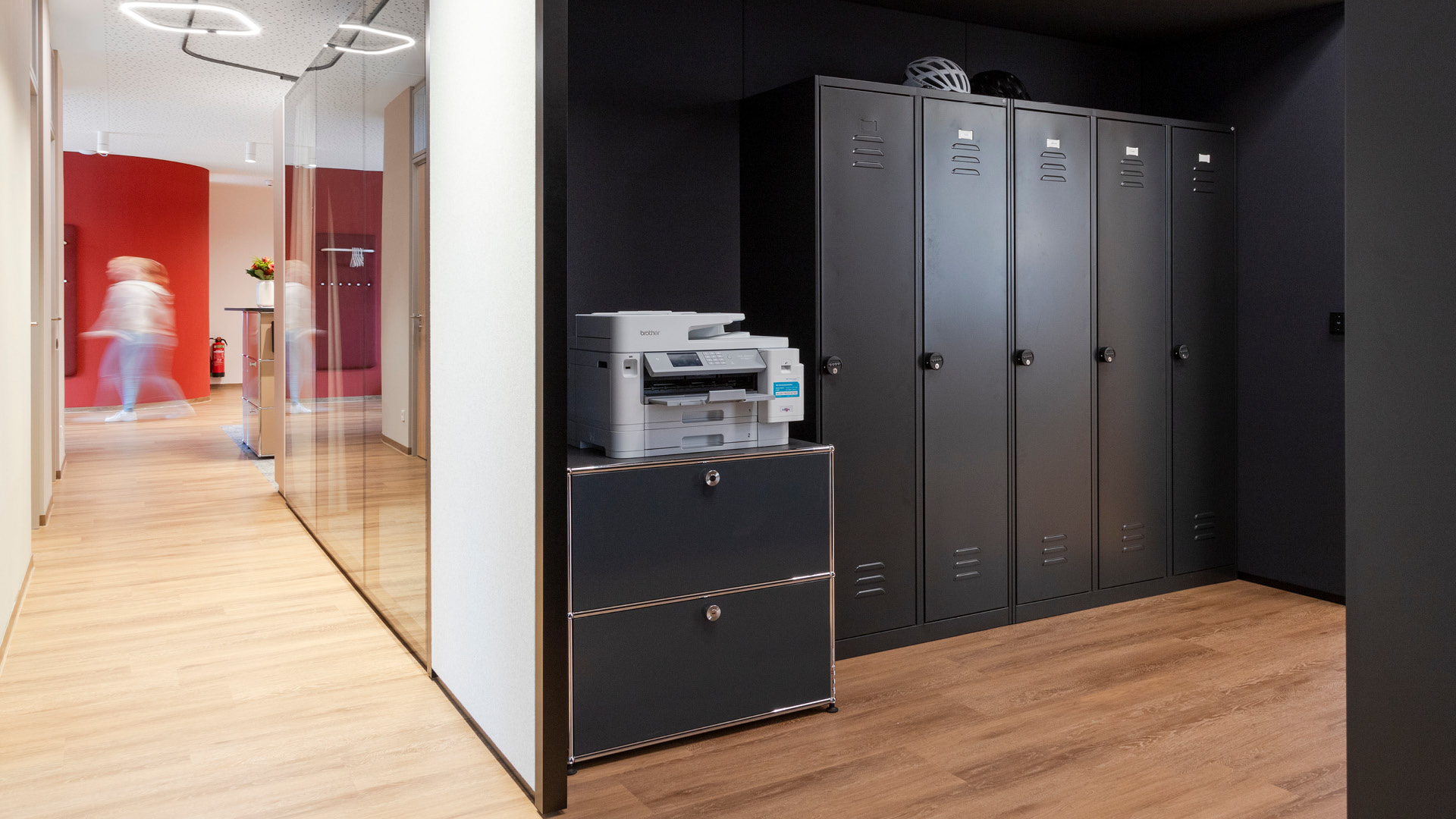 Mitarbeiterbereich mit schwarzen Spinden, USM Haller Druckerschrank und angrenzendem Flur.