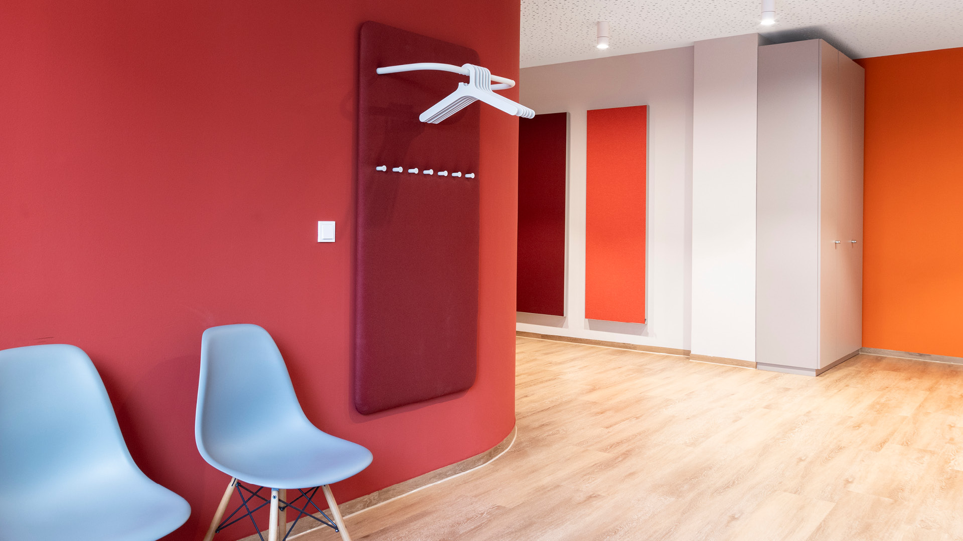 Wartebereich mit Garderobe, Sitzgelegenheiten und farbigen Akustikelementen.