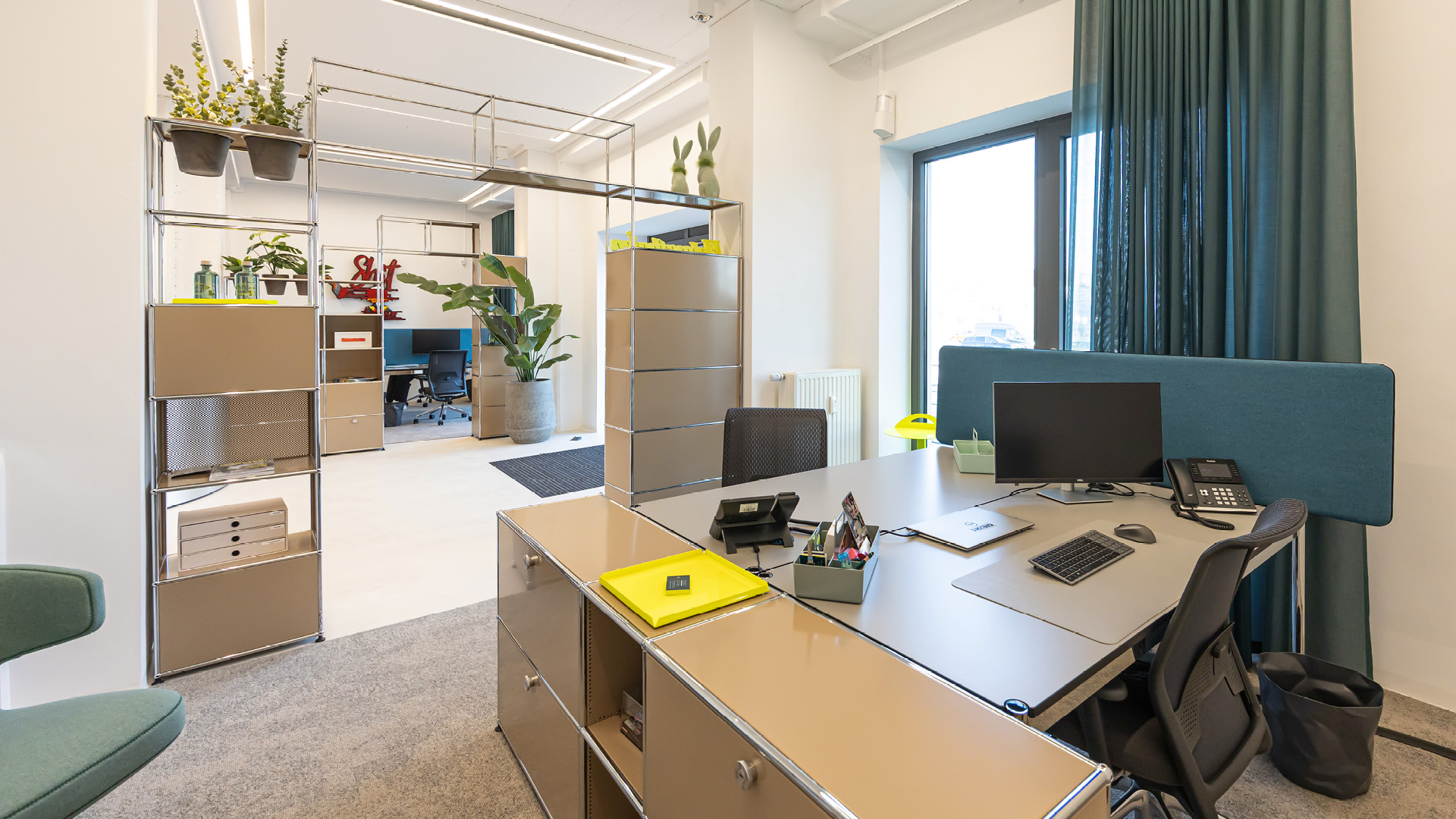 USM Haller Arbeitsplatz im Referenzprojekt Heimathafen Immobilien in Münster mit integriertem Stauraum, Sichtschutz-Panel und offener Zonierung durch Regalsysteme für strukturierte Büroarbeit.
