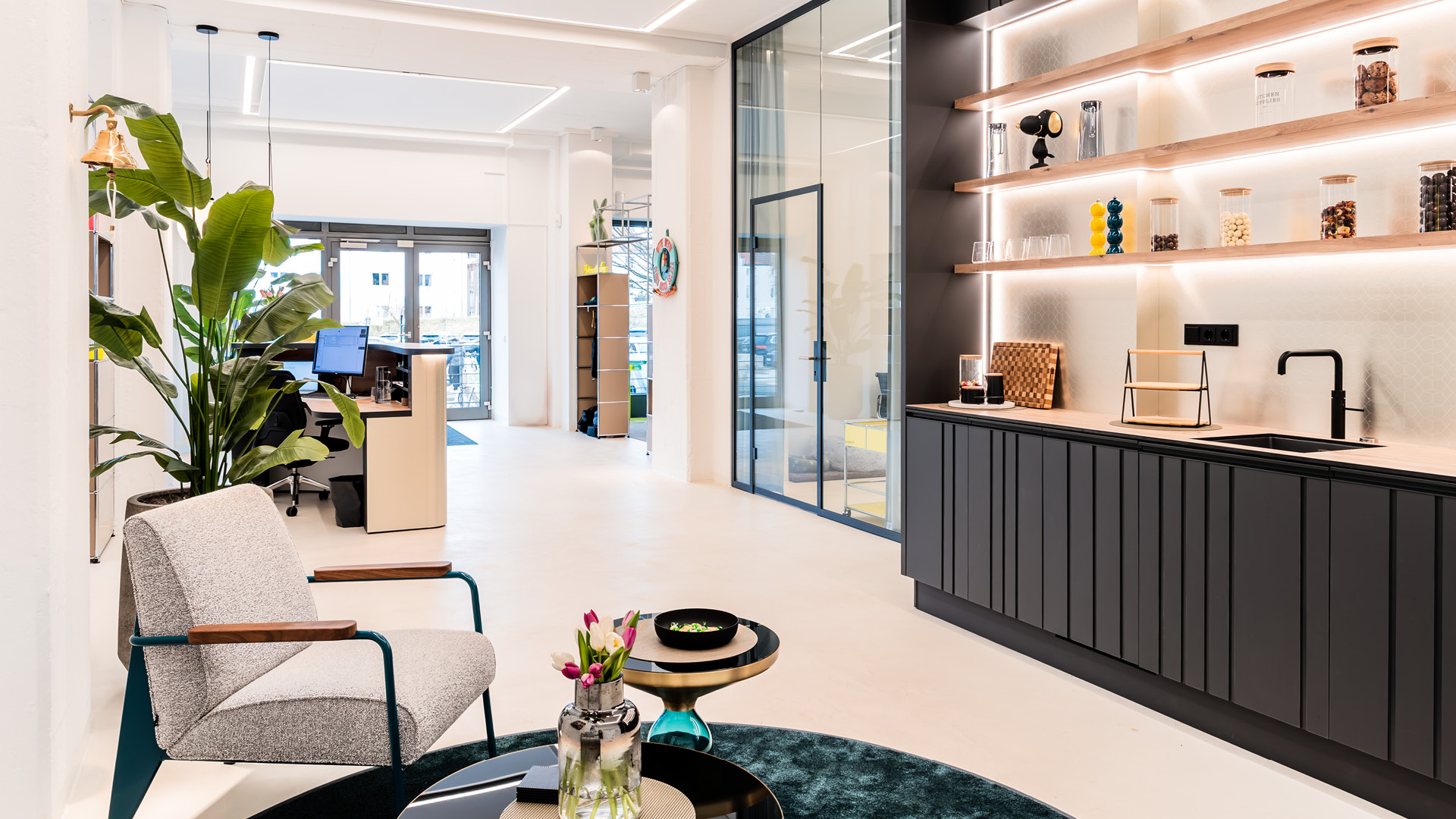 Heller, modern gestalteter Büro- und Empfangsbereich im Referenzprojekt Heimathafen Immobilien in Münster mit offener Teeküche, Glasbüros, Arbeitsplatz und stilvoller Lounge-Zone für zeitgemäßes Arbeiten.