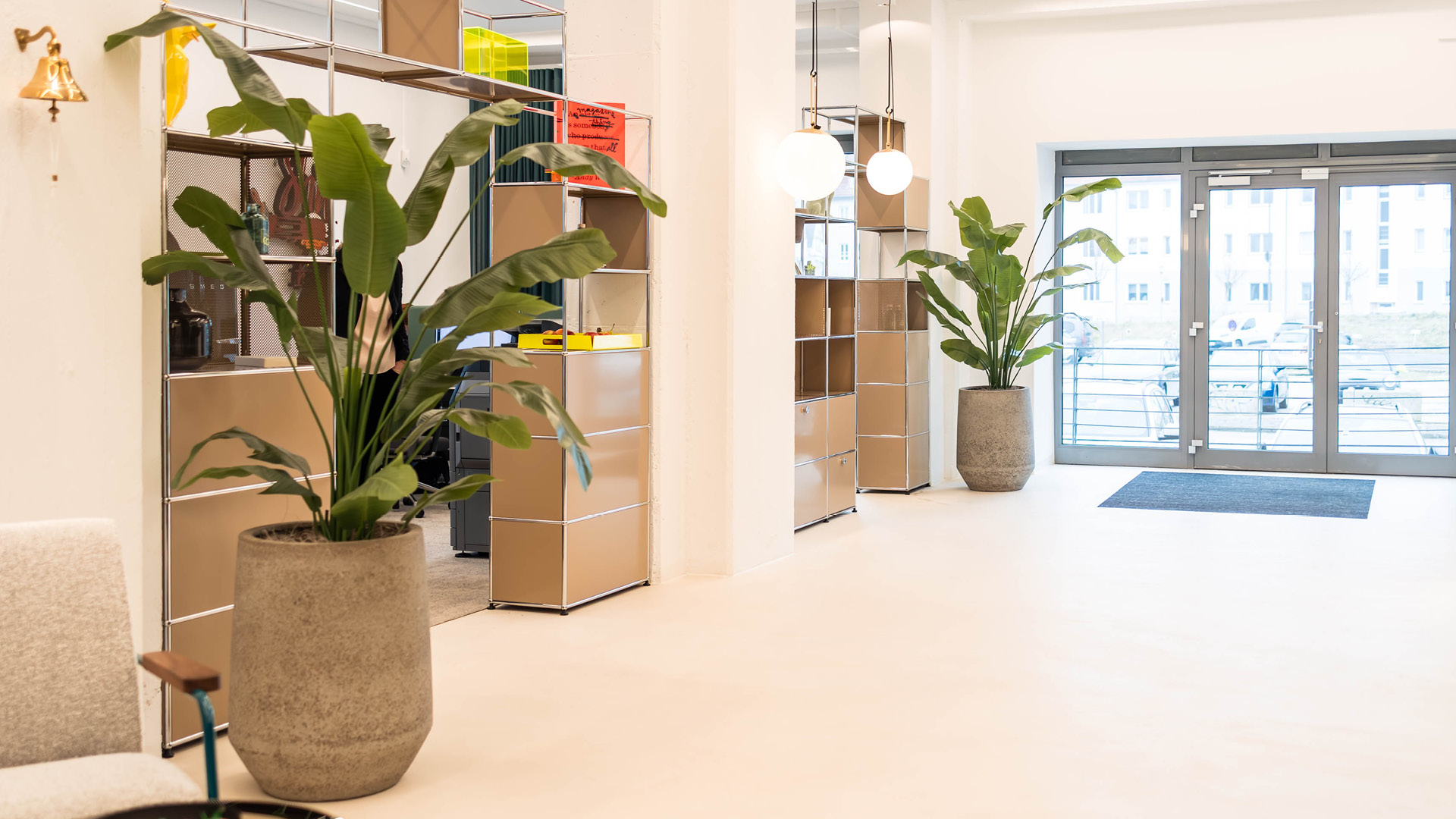 USM Haller Regalsysteme zur offenen Zonierung im Referenzprojekt Heimathafen Immobilien in Münster, mit integrierten Pflanzen, Empfangsbereich und klar strukturiertem Eingangs- und Arbeitsbereich.