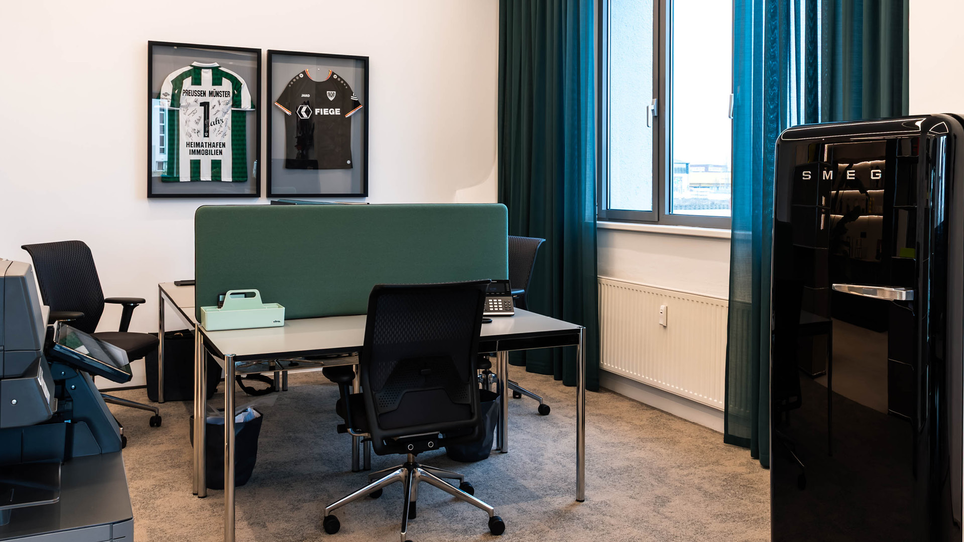 USM Haller Arbeitsplatz im Referenzprojekt Heimathafen Immobilien in Münster, mit strukturiertem Desk-Setup, Sichtschutz-Panel und klar zoniertem Bürobereich für konzentriertes Arbeiten.