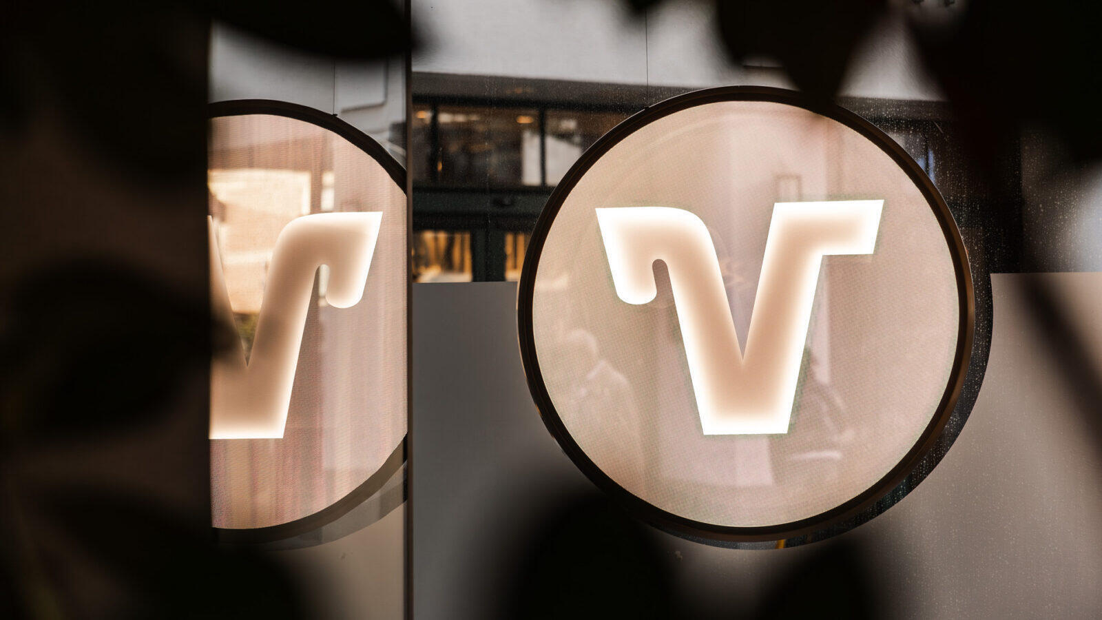 Beleuchtetes Logo der Volksbank Münsterland eG an der Wand als modernes Designelement im Fenster der Pop-Up-Filiale.